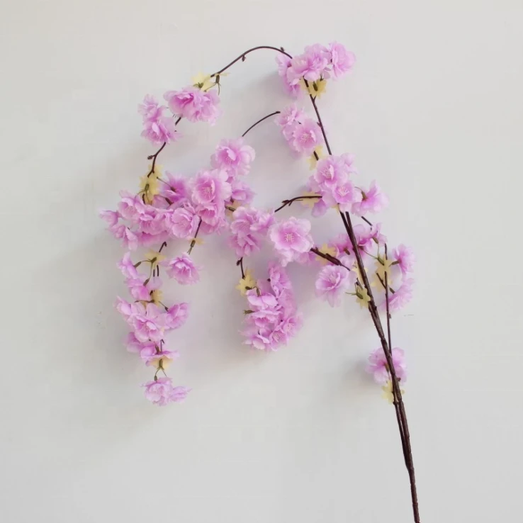 Pink artificial blossoms along slender brown branches against a pale wall