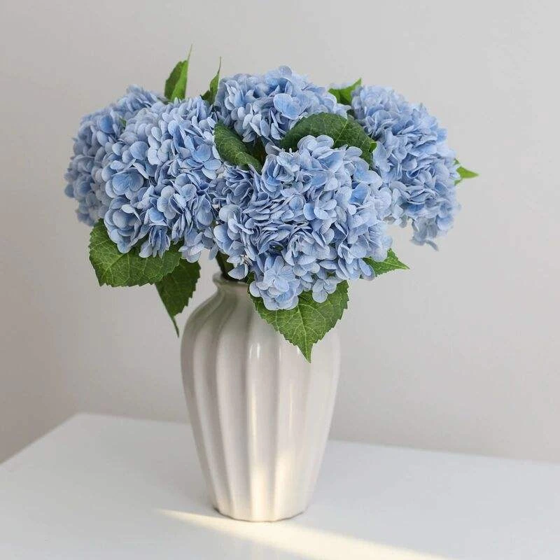Blue artificial hydrangeas with textured petals arranged in a white vase