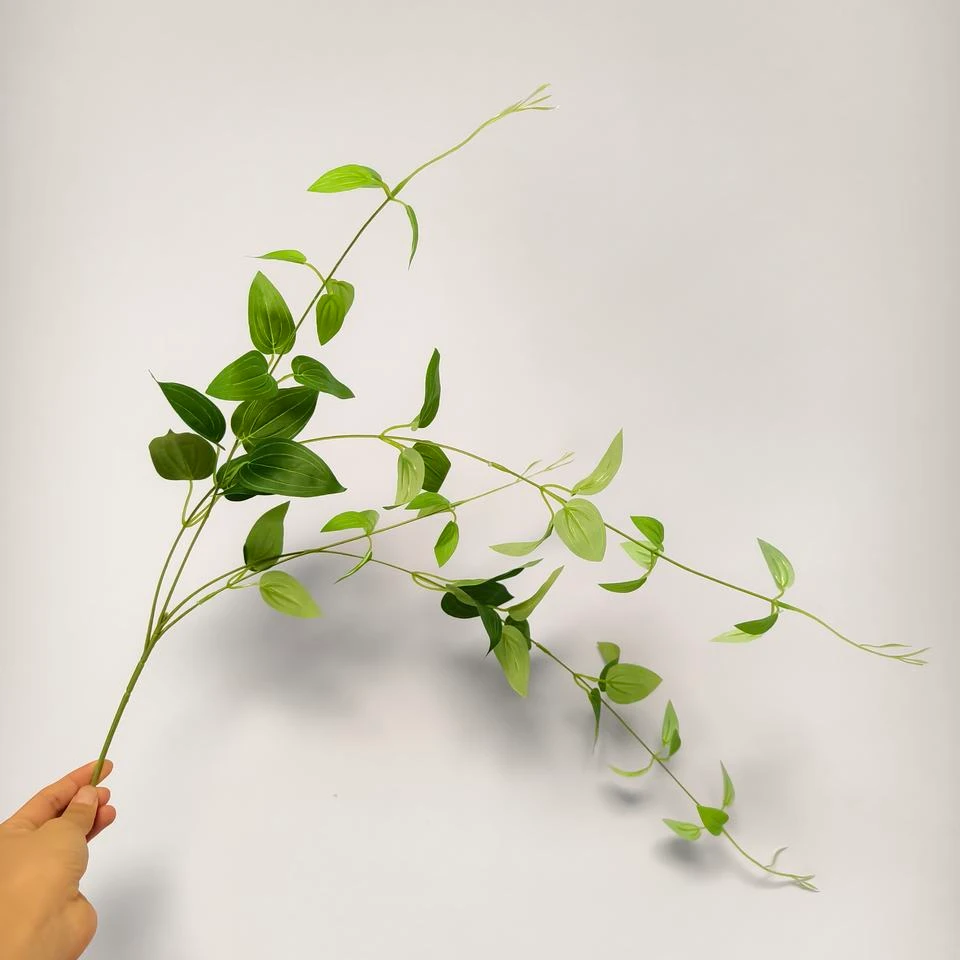 Delicate green artificial clematis vine held against a neutral background