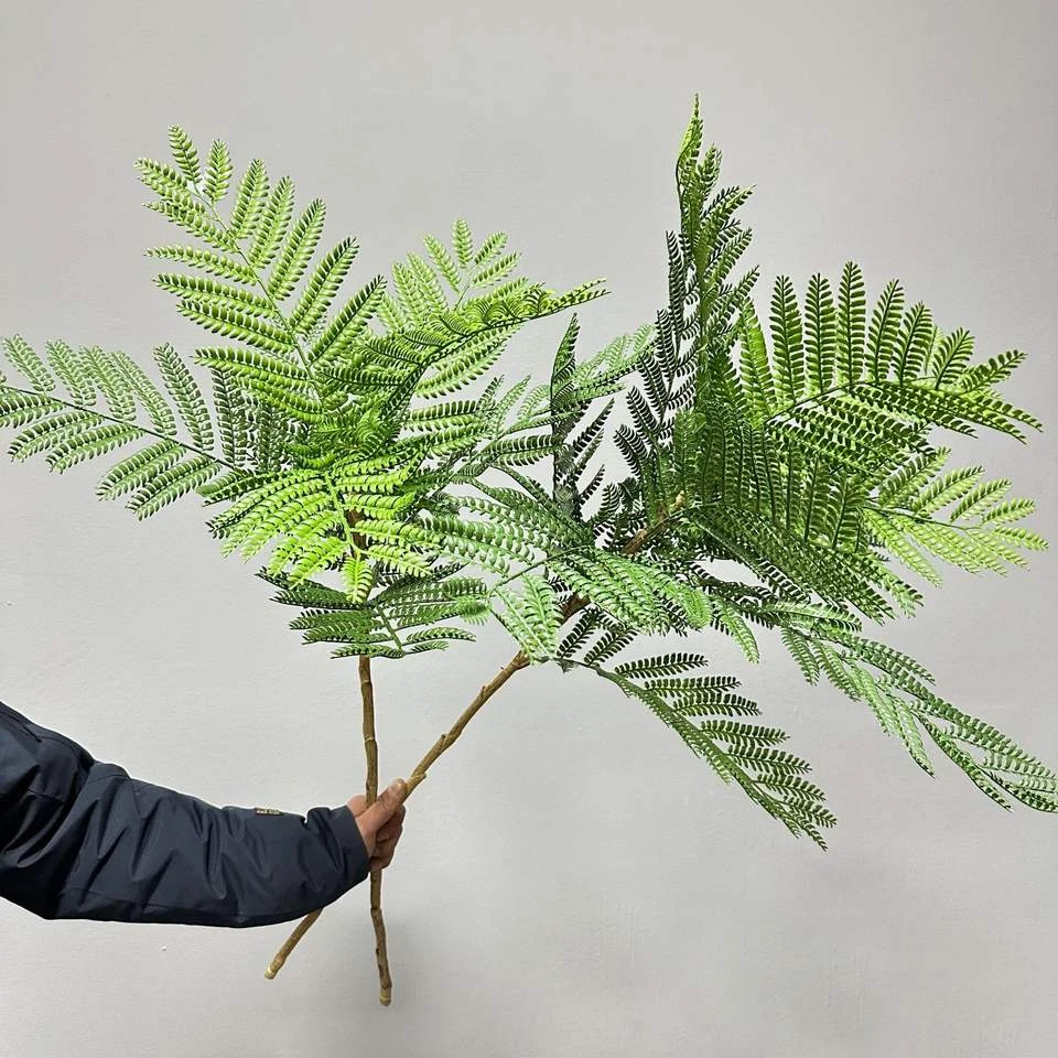 Artificial fern-like jacaranda foliage branch held by its bare stem