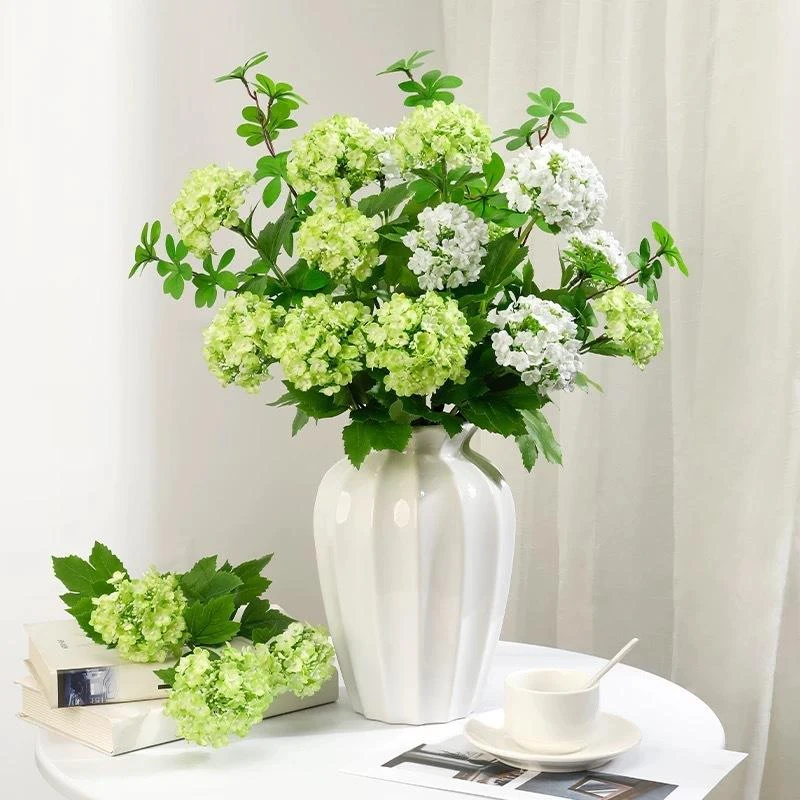 Small white and green artificial hydrangea flowers styled in a tall white vase