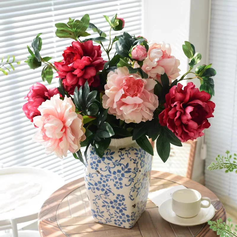 Pink and red artificial peonies arranged in a patterned vase