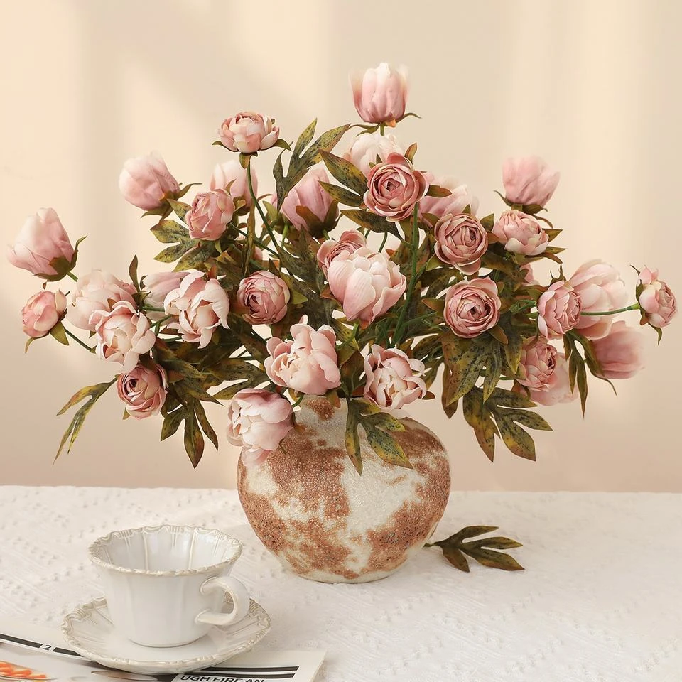 Muted pink artificial rose-style flowers and buds arranged in a patterned vase