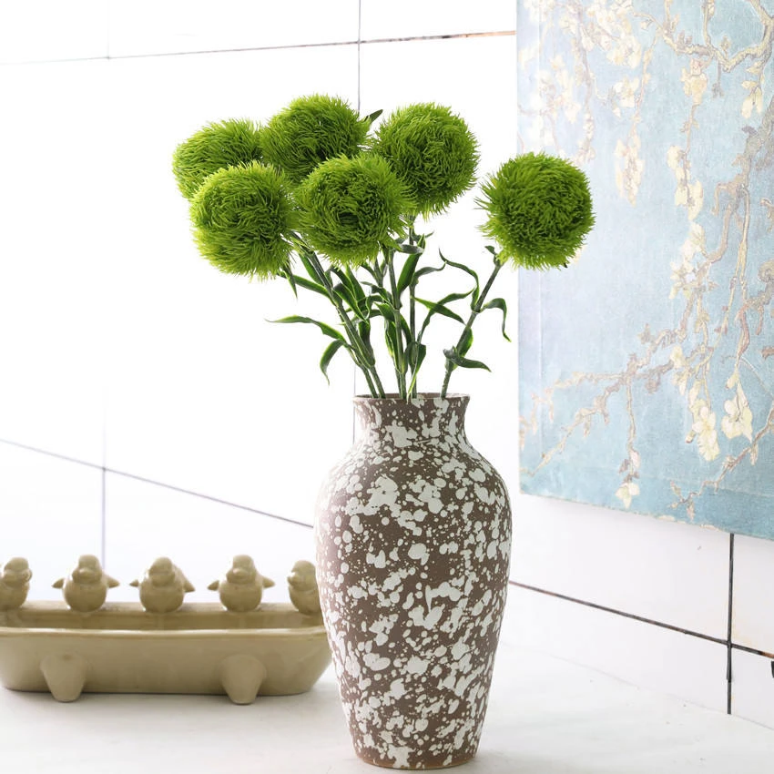 Green rounded artificial dianthus flowers arranged in a patterned vase