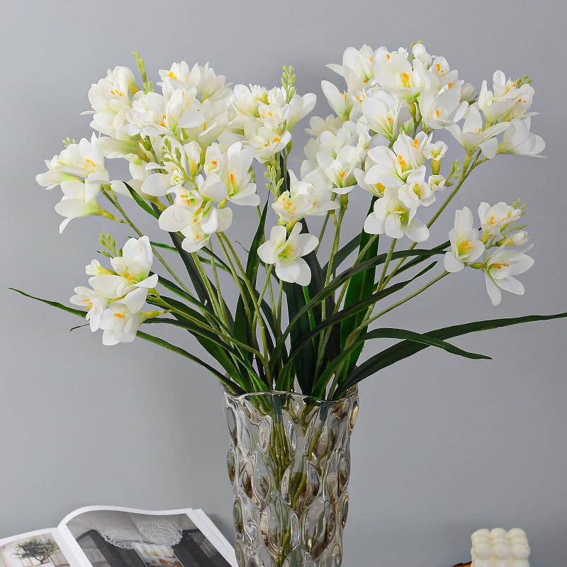 White artificial freesia flowers displayed in a glass vase